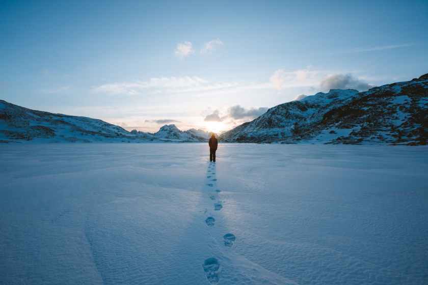 person walking in snow field near mountain cliff covered with snow
